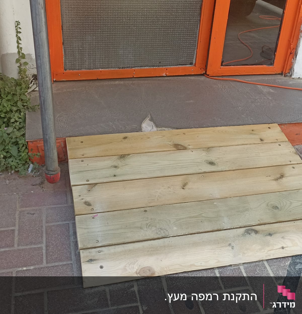 רמפת עץ על מדרכה ליד דלת כתומה
